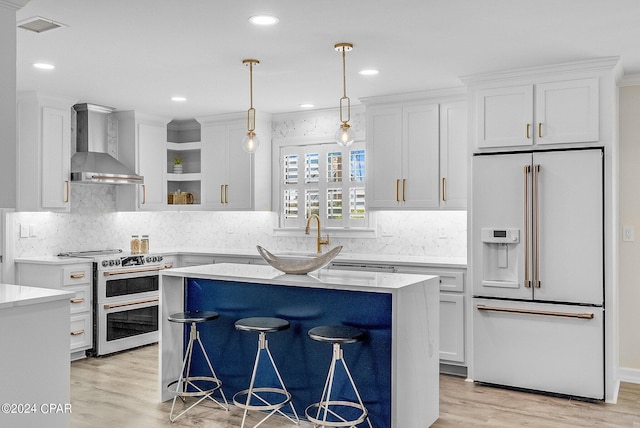 kitchen featuring high end white fridge, electric range oven, wall chimney range hood, white cabinetry, and a breakfast bar