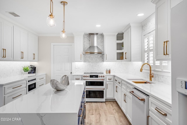 kitchen with pendant lighting, sink, white cabinets, wall chimney range hood, and stainless steel appliances