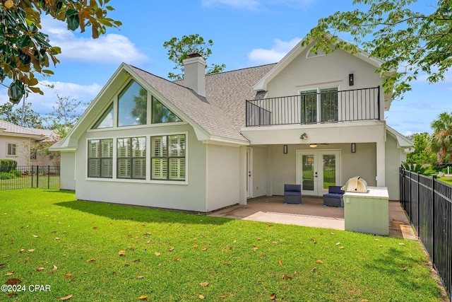 rear view of property with a patio, a balcony, a lawn, and french doors