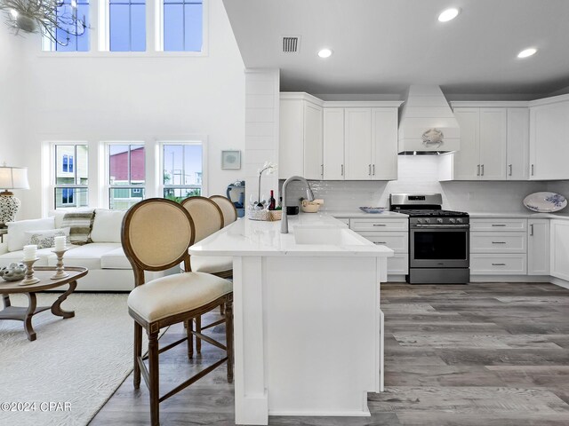 kitchen featuring custom exhaust hood, kitchen peninsula, stainless steel range with gas cooktop, white cabinetry, and hardwood / wood-style floors