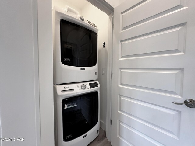 laundry area with stacked washer / drying machine and hardwood / wood-style flooring