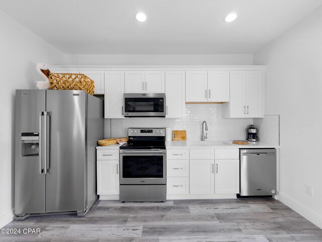 kitchen with light countertops, backsplash, a sink, stainless steel appliances, and white cabinets