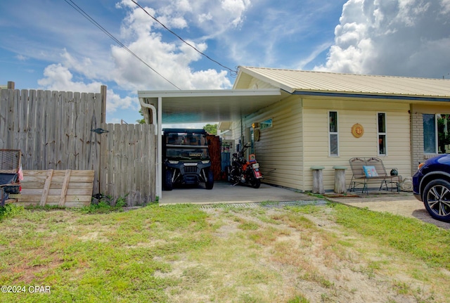 view of side of property with metal roof, an attached carport, brick siding, fence, and driveway