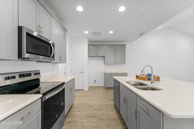 kitchen with an island with sink, light hardwood / wood-style floors, gray cabinetry, appliances with stainless steel finishes, and sink