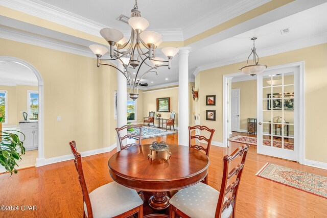 dining space with light hardwood / wood-style flooring, ornamental molding, an inviting chandelier, and ornate columns