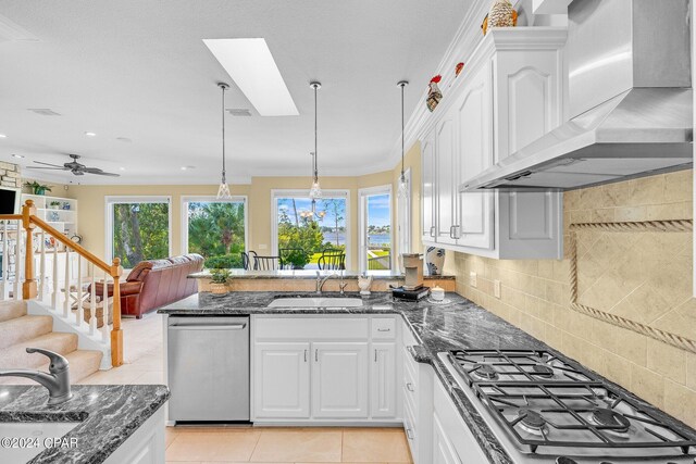 kitchen featuring a skylight, white cabinets, appliances with stainless steel finishes, wall chimney exhaust hood, and ceiling fan