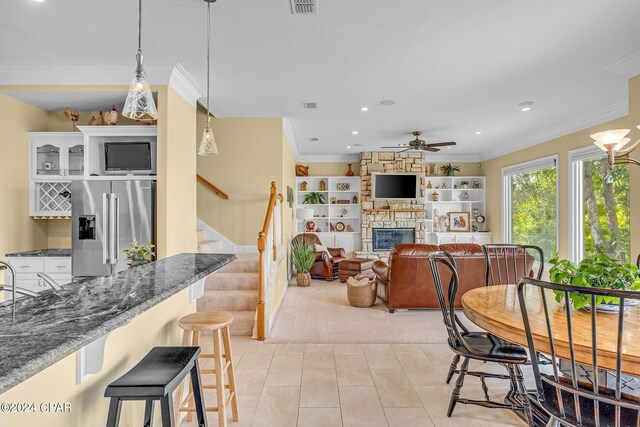 tiled dining space featuring a fireplace, crown molding, and ceiling fan