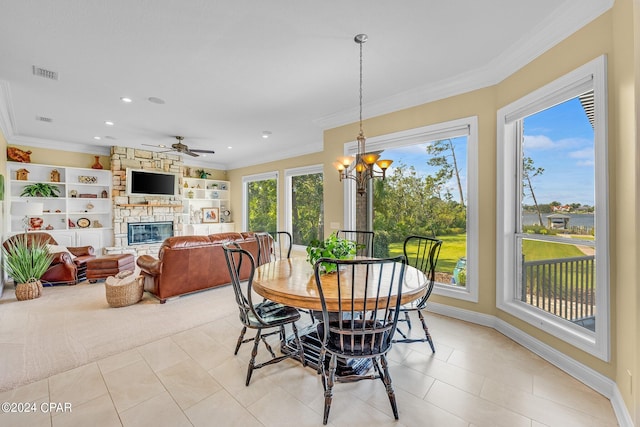 tiled dining area with built in features, ceiling fan with notable chandelier, crown molding, and a stone fireplace