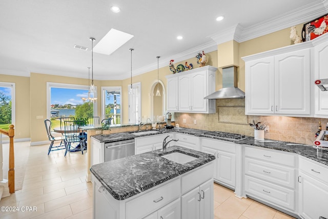 kitchen with dark stone countertops, pendant lighting, a skylight, kitchen peninsula, and wall chimney exhaust hood