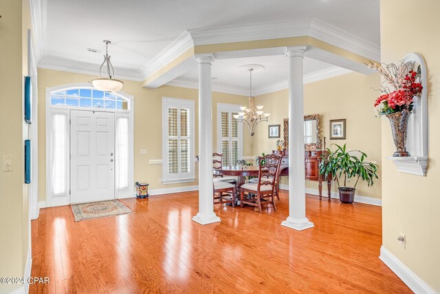 foyer entrance featuring crown molding, ornate columns, a notable chandelier, and light hardwood / wood-style floors