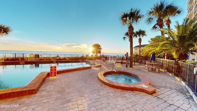 pool at dusk with a water view, a community hot tub, and a patio