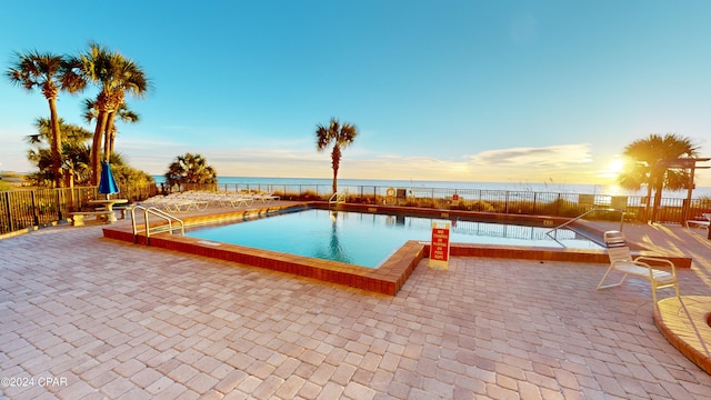 pool at dusk with a water view and a patio area