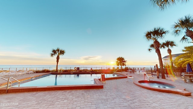 pool at dusk featuring a water view, a patio, and a hot tub