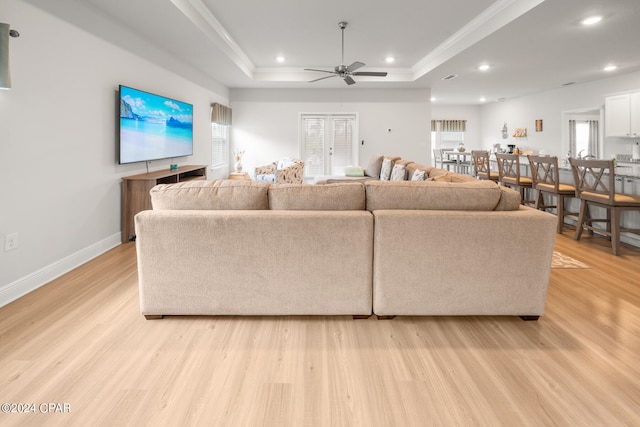 living room featuring light wood-type flooring, a healthy amount of sunlight, ceiling fan, and a tray ceiling