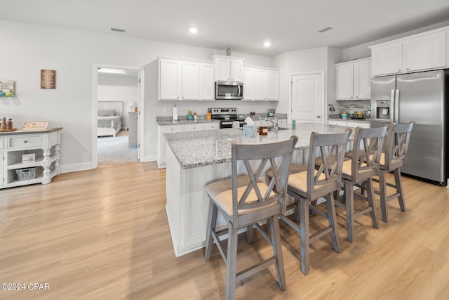 kitchen featuring light stone counters, stainless steel appliances, a kitchen bar, and white cabinetry