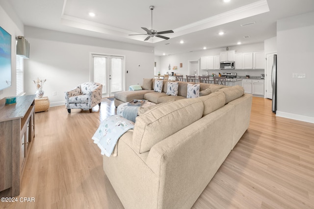 living room with ceiling fan, light wood-type flooring, crown molding, and a tray ceiling