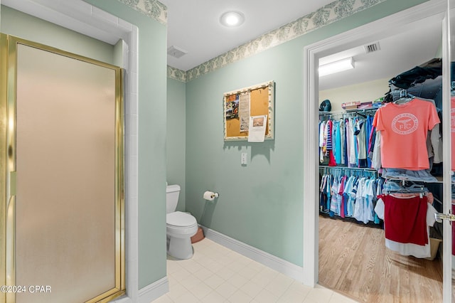 bathroom with hardwood / wood-style floors, toilet, and a shower with door