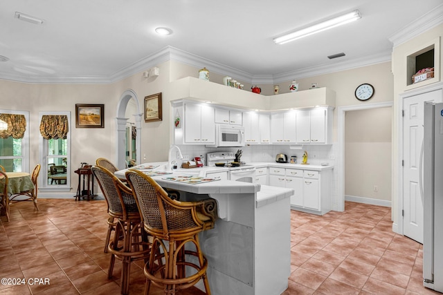 kitchen with tasteful backsplash, white cabinets, kitchen peninsula, white appliances, and crown molding