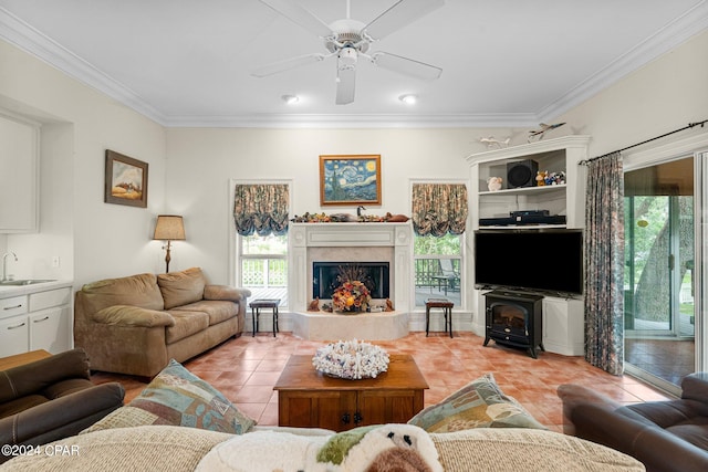 tiled living room with a fireplace, a wood stove, ceiling fan, ornamental molding, and sink