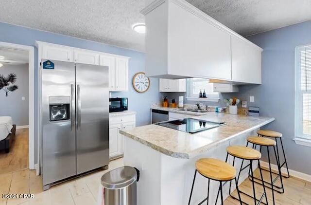 kitchen with kitchen peninsula, a textured ceiling, white cabinetry, black appliances, and a kitchen breakfast bar