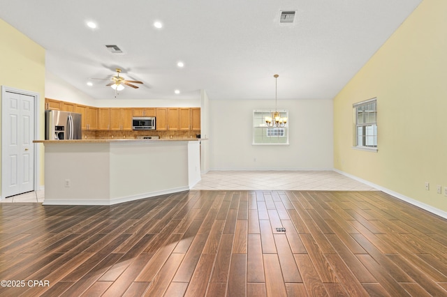 unfurnished living room featuring ceiling fan with notable chandelier, lofted ceiling, and hardwood / wood-style flooring