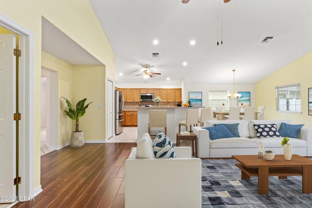 living room with ceiling fan with notable chandelier, dark hardwood / wood-style flooring, and lofted ceiling