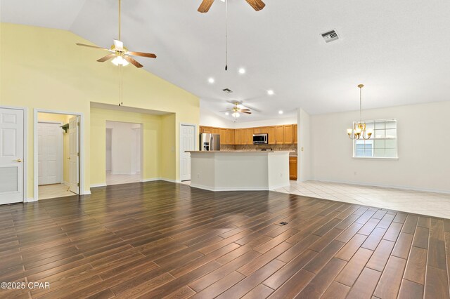 unfurnished living room featuring ceiling fan with notable chandelier, high vaulted ceiling, and dark wood-type flooring