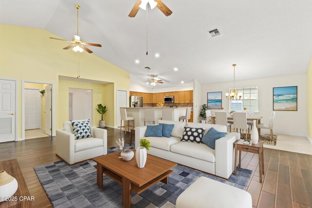 living room featuring ceiling fan with notable chandelier, high vaulted ceiling, and dark wood-type flooring