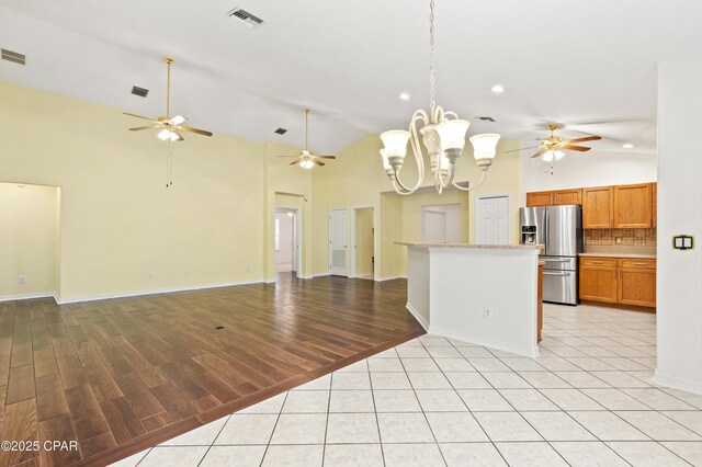 kitchen with light hardwood / wood-style flooring, stainless steel refrigerator with ice dispenser, ceiling fan with notable chandelier, high vaulted ceiling, and tasteful backsplash