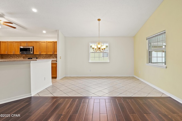 kitchen featuring decorative backsplash, light tile patterned floors, hanging light fixtures, and ceiling fan with notable chandelier