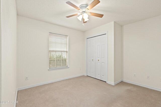 unfurnished bedroom with ceiling fan, a closet, light carpet, and a textured ceiling