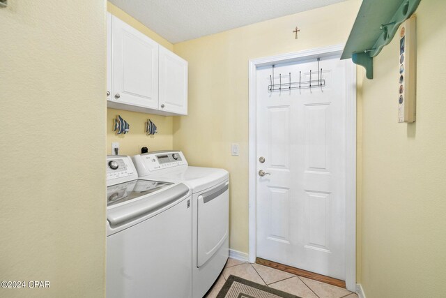 laundry area featuring washing machine and clothes dryer, light tile patterned floors, cabinets, and a textured ceiling