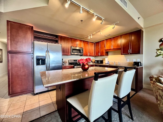 kitchen with stainless steel appliances, a kitchen breakfast bar, light tile patterned floors, a kitchen island, and stone countertops