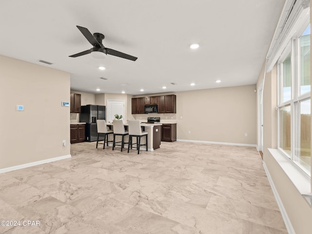 kitchen featuring a breakfast bar area, a center island, ceiling fan, black appliances, and dark brown cabinets