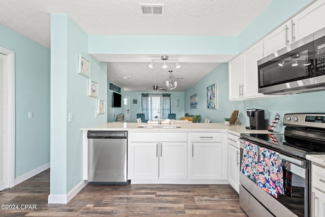 kitchen with dark wood-type flooring, white cabinets, kitchen peninsula, stainless steel appliances, and sink