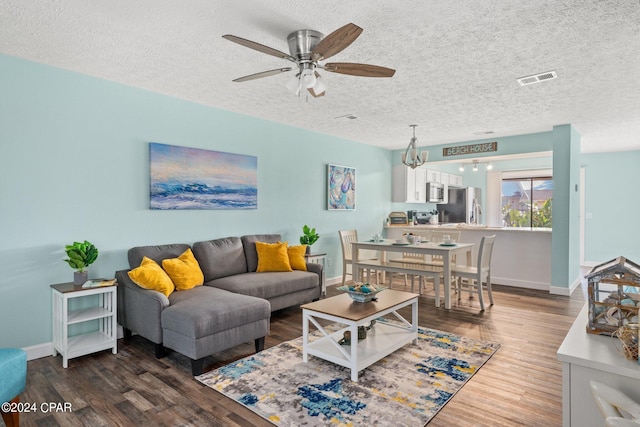 living room featuring a textured ceiling, ceiling fan with notable chandelier, and dark wood-type flooring