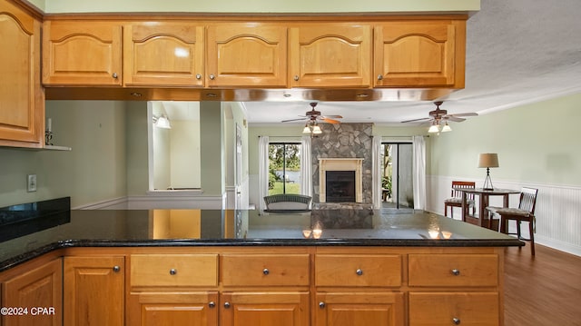 kitchen with dark stone countertops, ceiling fan, ornamental molding, and a stone fireplace