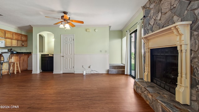 living room featuring crown molding, dark wood-type flooring, ceiling fan, and a stone fireplace