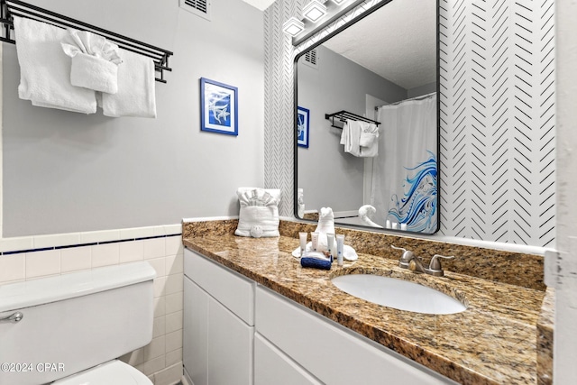 bathroom with walk in shower, toilet, tile walls, vanity, and a textured ceiling