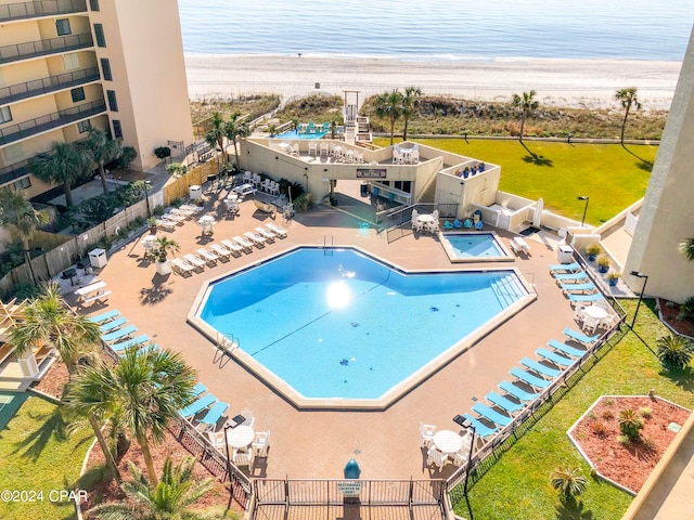 view of pool featuring a water view, a lawn, a view of the beach, and a patio area