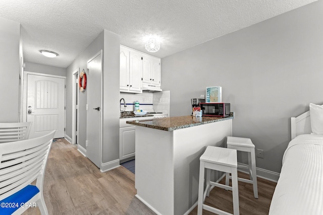 kitchen with light wood-type flooring, white cabinetry, kitchen peninsula, and a textured ceiling