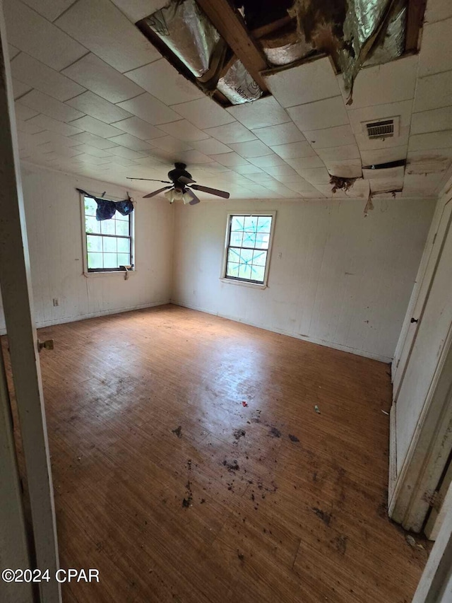 empty room with a wealth of natural light, wood-type flooring, and ceiling fan