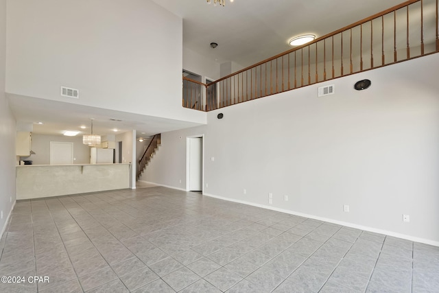 unfurnished living room featuring an inviting chandelier, light tile patterned floors, and a high ceiling