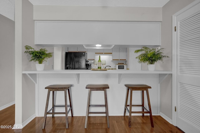 kitchen featuring white cabinets, a kitchen bar, kitchen peninsula, dark wood-type flooring, and black refrigerator with ice dispenser