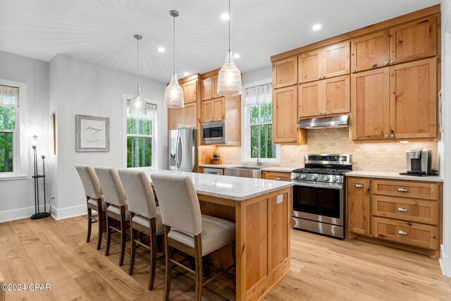 kitchen with a center island, hanging light fixtures, stainless steel appliances, light hardwood / wood-style flooring, and a breakfast bar