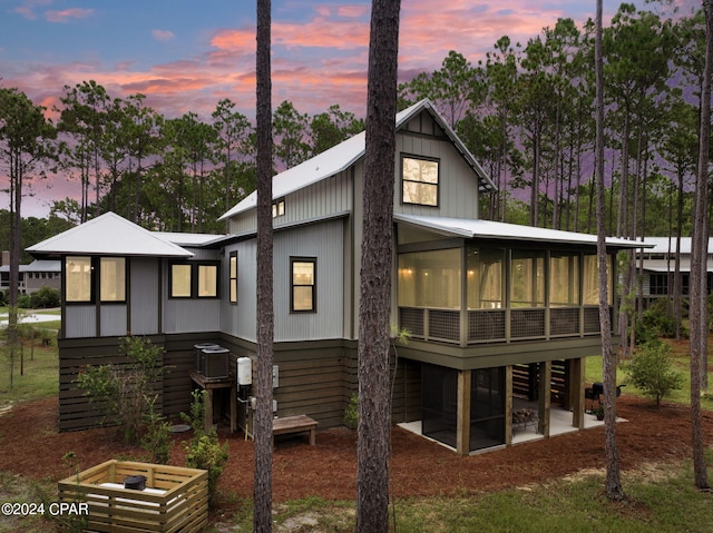 back of house at dusk featuring a patio area, central air condition unit, and a sunroom