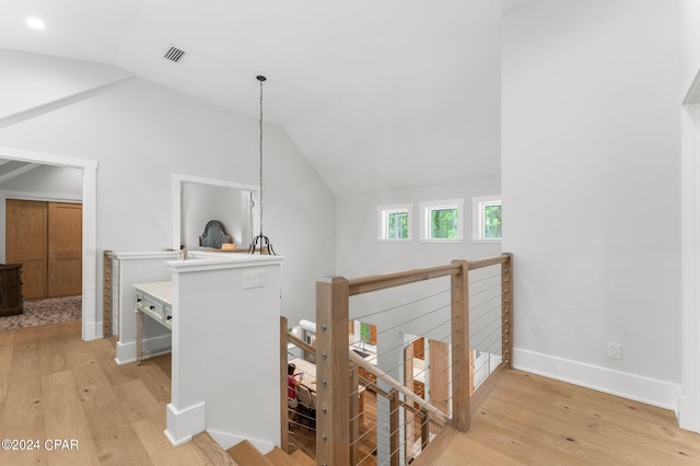 hall featuring visible vents, light wood-type flooring, an upstairs landing, and lofted ceiling