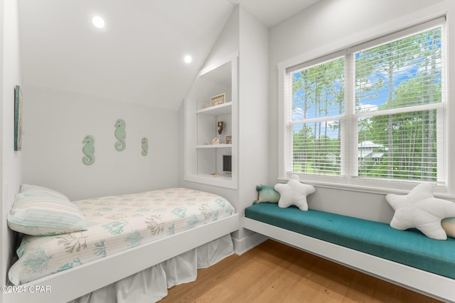 bedroom with wood finished floors, baseboards, vaulted ceiling, and multiple windows