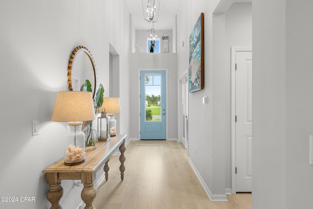 foyer entrance with light hardwood / wood-style flooring, a towering ceiling, and a chandelier