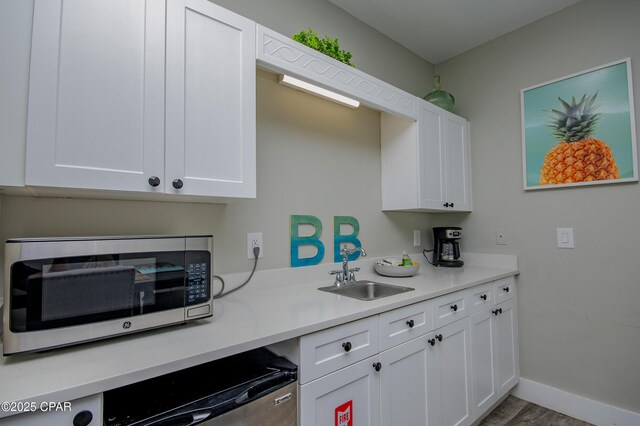 112 Riviera Dr, Panama City Beach, FL 32413 - kitchen featuring stainless steel microwave, a sink, white cabinetry, light countertops, and wood finished floors